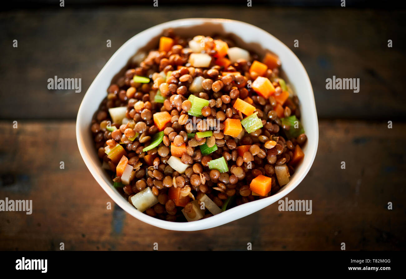 Tazón de rústica saludable lentejas cocidas y verduras ricas en proteínas y fibra dietética en una vista superior de una tabla Foto de stock