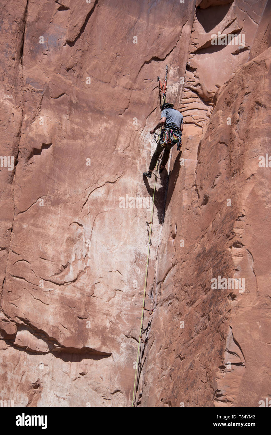 Escalador de roca libre hombre escalada solo hasta los asideros y los pies en los acantilados de arenisca roja para establecer pitones y cuerdas en Moab, Utah, EE.UU., 7 de mayo de 2019 Foto de stock