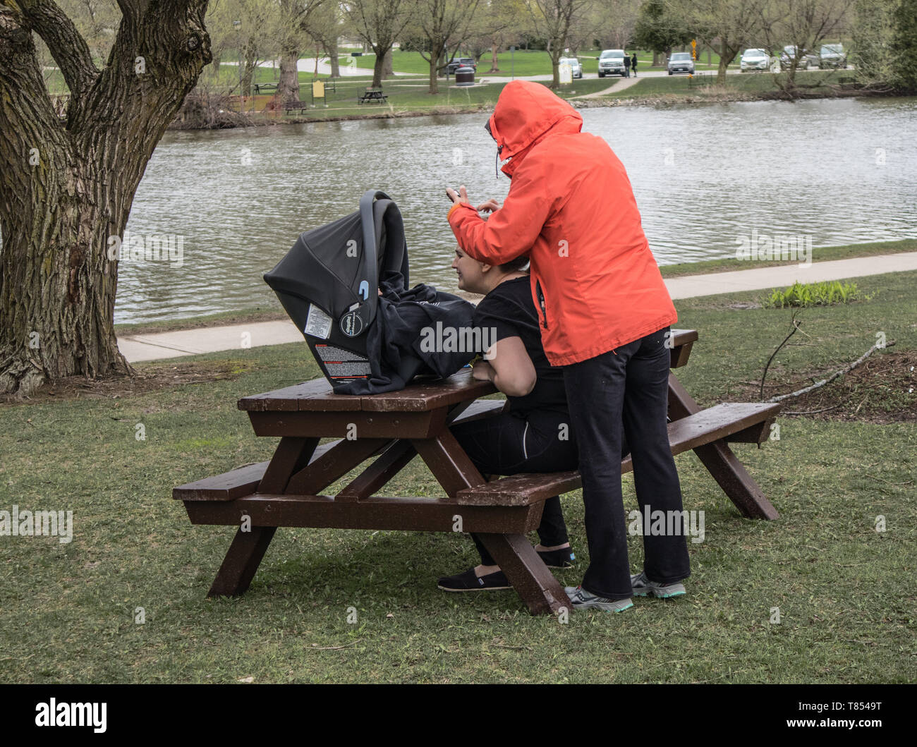 Dos mujeres y un niño en el parque en Stratford, Ontario. Una de ellas toma una fotografía del niño. Cool día gris. Foto de stock
