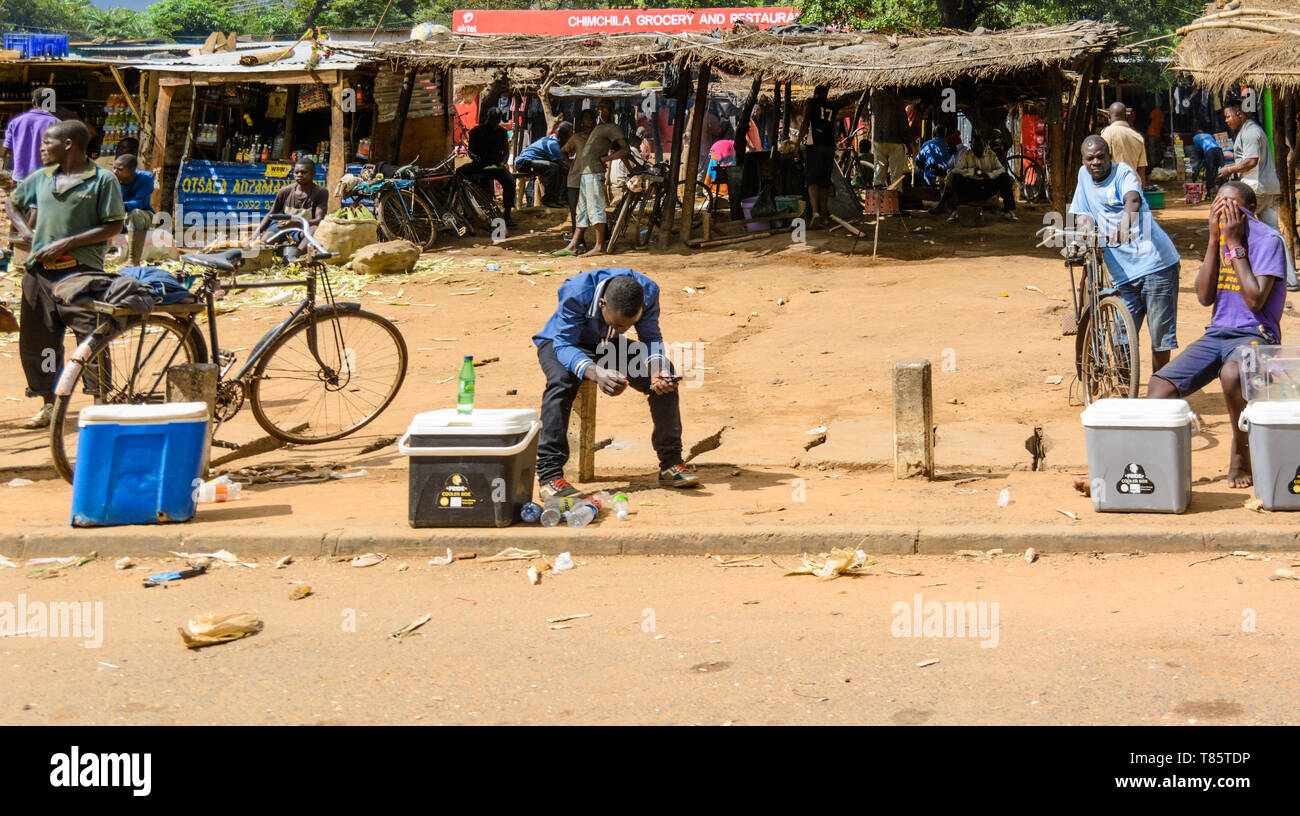 Hombre de Malawi vender bebidas gaseosas frías desde su caja refrigerada en frente de un mercado de transporte por carretera en la aldea de Malawi Foto de stock