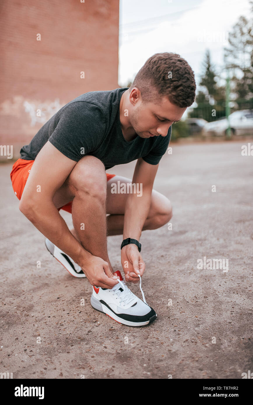 Atleta Masculino runner atarse los cordones de las zapatillas de deporte en  la ciudad en el aire fresco. Concepto de Fitness y entrenamiento, Smart  Watch Bracelet. Sportswear T-shirt cortos Fotografía de stock -