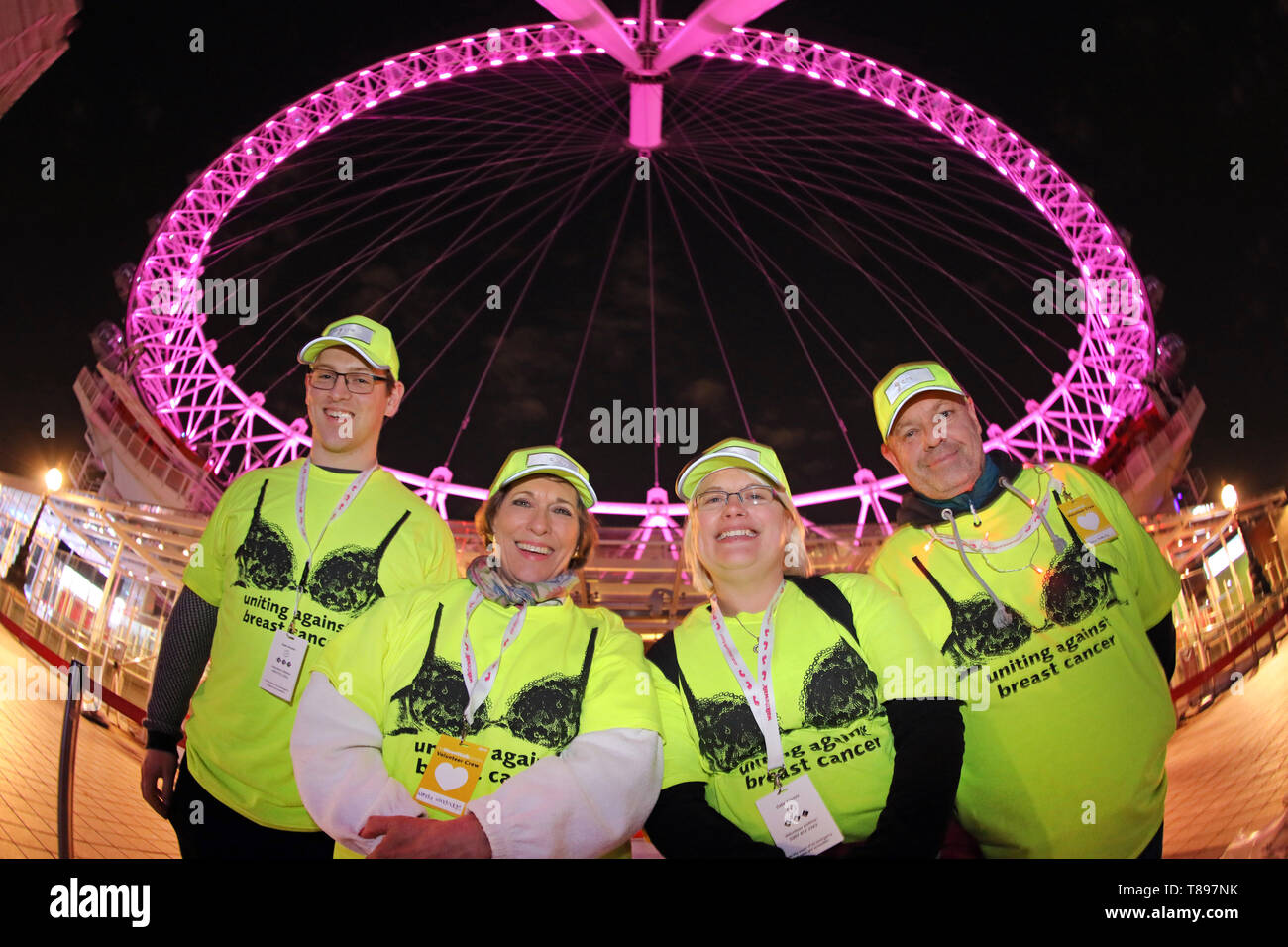 Londres, Reino Unido. El 11 de mayo de 2019. Un grupo de voluntarios en la parte delantera del Ojo de Londres que se convirtió rosa para el Caminar Moonwalk caridad marathon vistiendo bras, Londres, Reino Unido. Miles de personas caminaron una ronda completa o media maratón de Londres vistiendo bras para recaudar fondos y conciencia para el cáncer de mama caminata benéfica de la caminata, pasando por muchos lugares emblemáticos de Londres, algunas de las cuales estaban iluminadas de color rosa para la maratón. El tema de este año era Disco Inferno . Crédito: Paul Brown/Alamy Live News Foto de stock