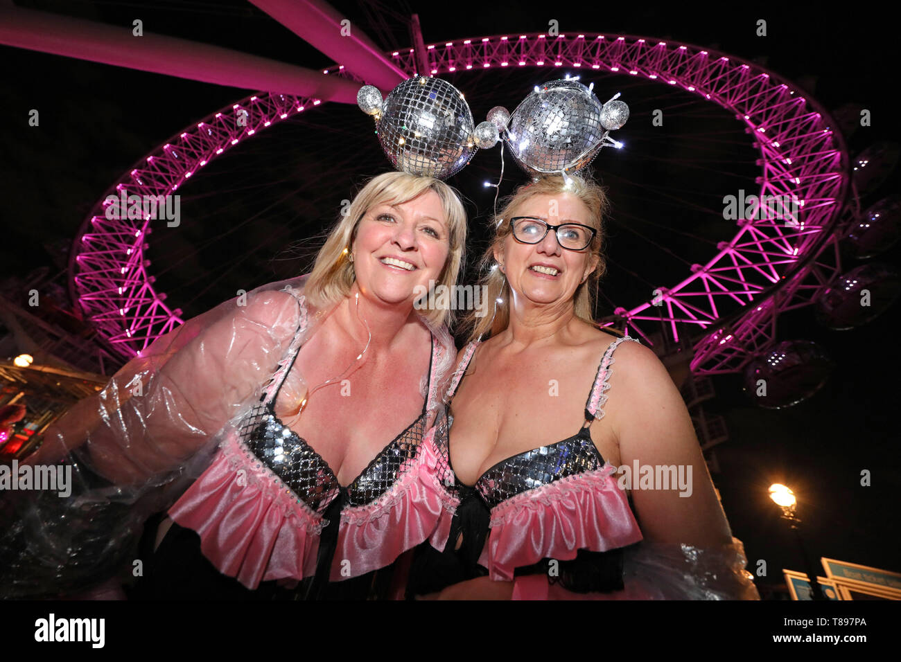 Londres, Reino Unido. El 11 de mayo de 2019. Los participantes en la parte delantera del Ojo de Londres que se convirtió rosa para el Caminar Moonwalk caridad marathon vistiendo bras, Londres, Reino Unido. Miles de personas caminaron una ronda completa o media maratón de Londres vistiendo bras para recaudar fondos y conciencia para el cáncer de mama caminata benéfica de la caminata, pasando por muchos lugares emblemáticos de Londres, algunas de las cuales estaban iluminadas de color rosa para la maratón. El tema de este año era Disco Inferno . Crédito: Paul Brown/Alamy Live News Foto de stock