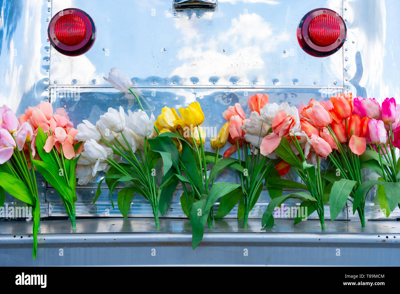 Vintage remolque camper con apartadero de aluminio y un paragolpes portón cubierto de flores de tulipán, representando la época hippie o un divertido estilo de vida. Foto de stock