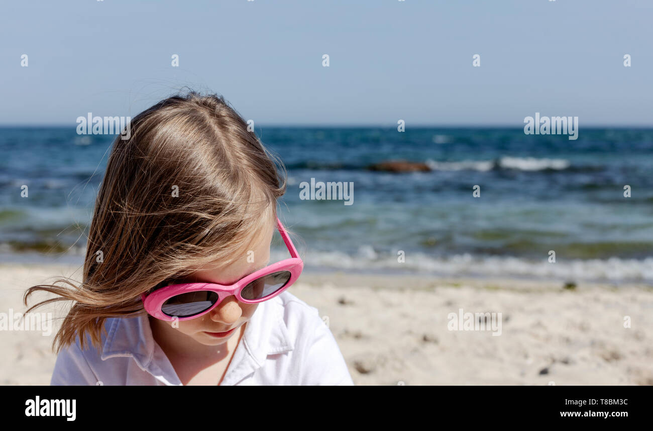 Funny Little Girl (7 años) en gafas de sol se encuentra en la playa. El enfoque selectivo. Foto de stock