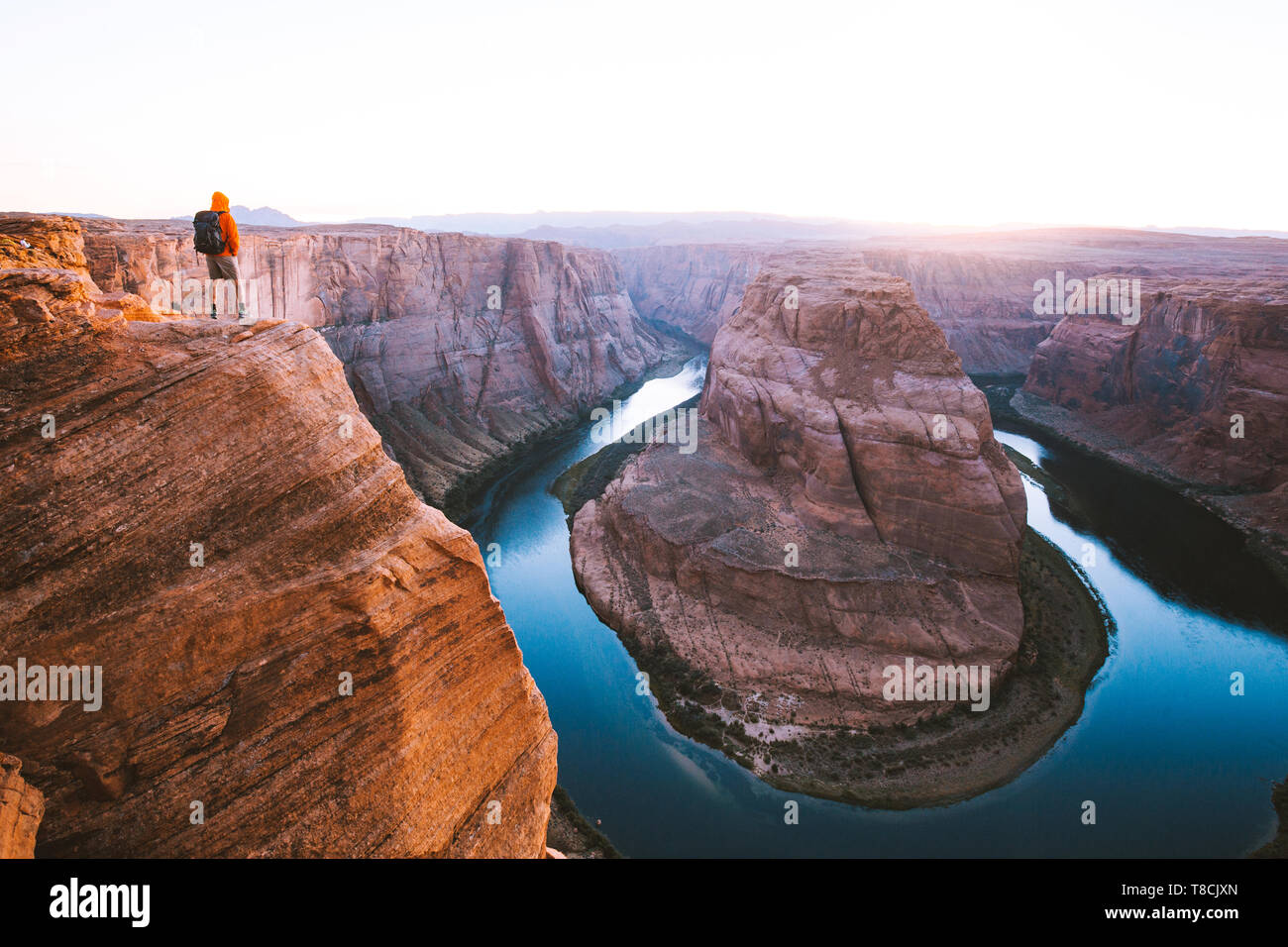 Un hombre caminante está de pie sobre acantilados disfrutando de la hermosa vista del río Colorado fluye a la famosa curva de herradura al atardecer, Arizona, EE.UU. Foto de stock