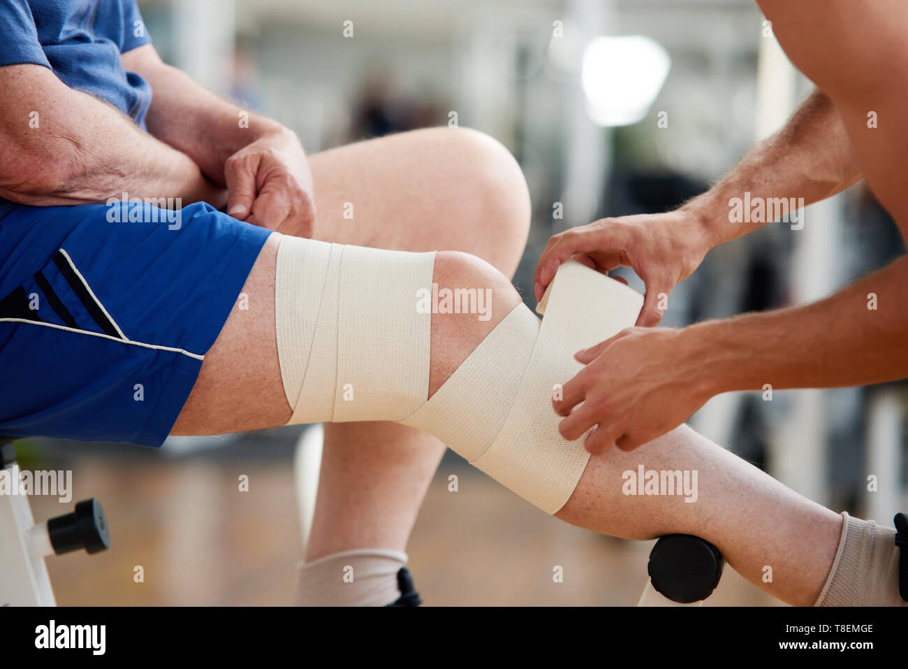 Hombre senior con vendaje en la pierna después de una lesión en el  gimnasio. Macho fijo manos venda elástica en la pierna lesionada  masculinos. El deporte y la salud Fotografía de stock -