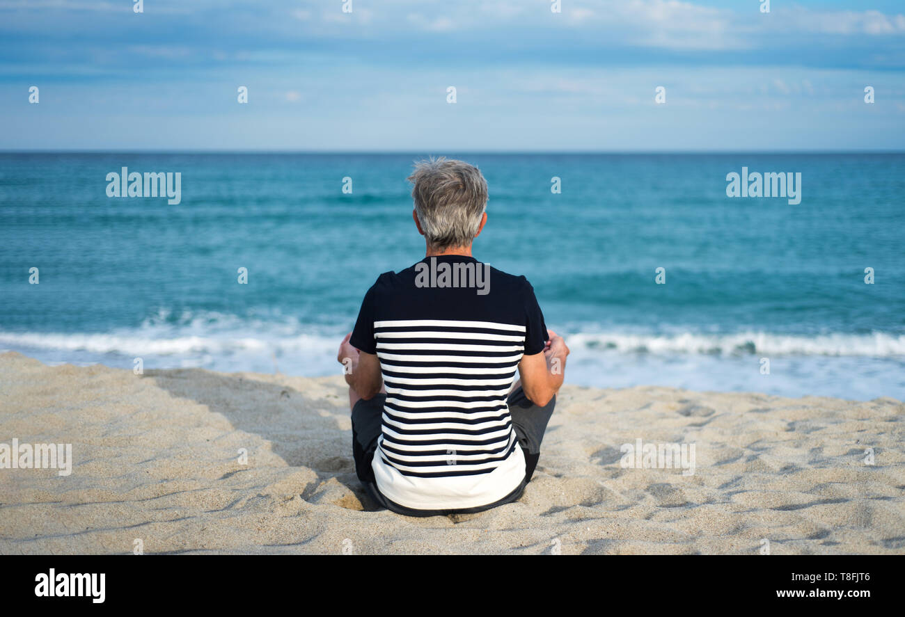 Hombre Senior meditando en la playa, vacaciones de verano entrenar Foto de stock