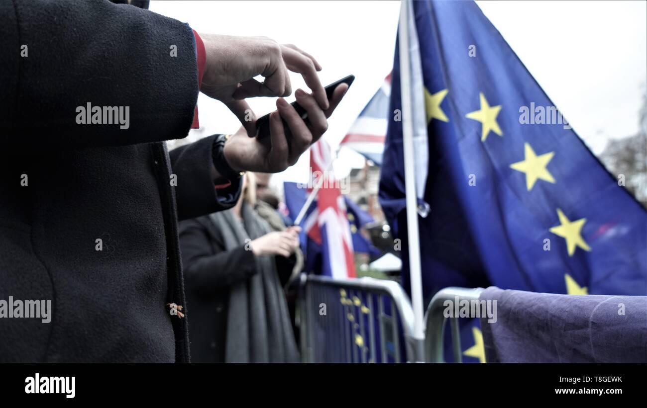 Hombre sujetando un teléfono móvil junto a una bandera de la UE durante la protesta Brexit y las elecciones de la UE. Foto de stock