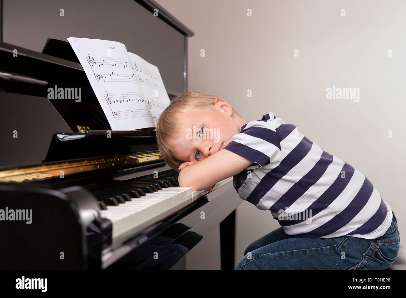 Niño de 4 años, sentado cansado delante del piano Foto de stock