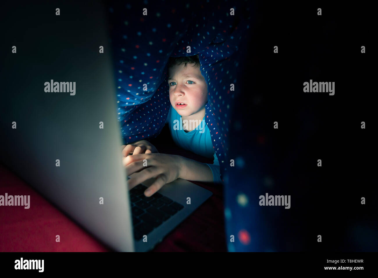 Boy secretamente usando el Internet en la cama Foto de stock