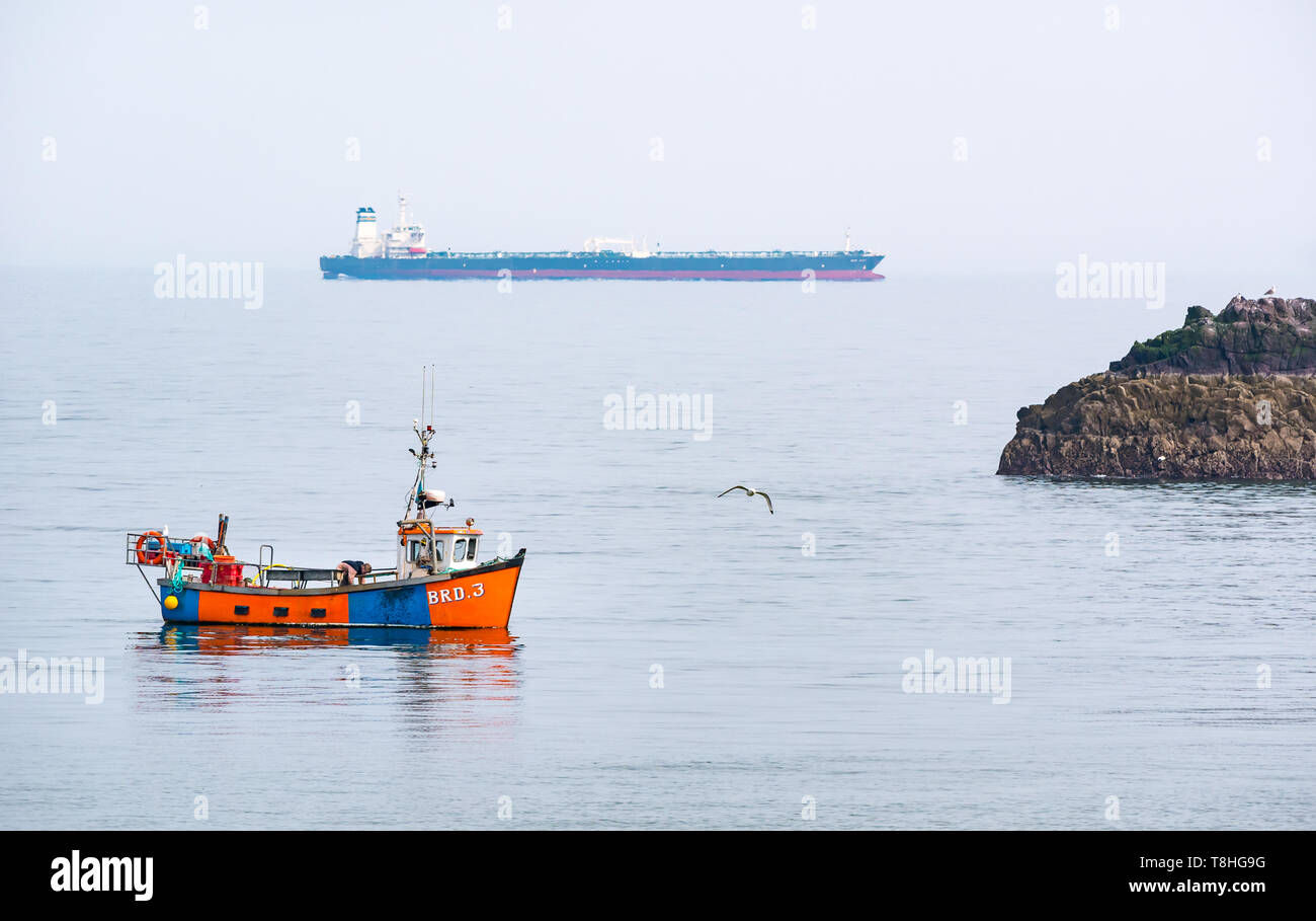 Dunbar barco pesquero en el mar tranquilo junto a la pequeña isla rocosa con aves marinas, petrolero en el horizonte, el Firth of Forth, East Lothian, Escocia, Reino Unido Foto de stock