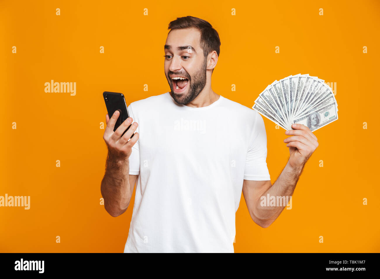 Foto de hombre caucásico 30s en ropa casual la celebración de teléfono celular y ventilador de dinero aislado sobre fondo amarillo Foto de stock