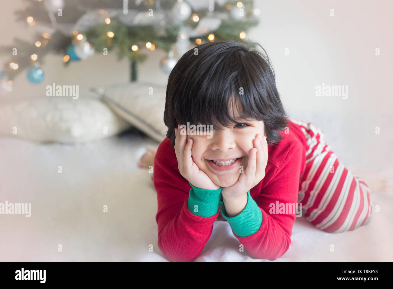 Muchacho bonito sentarse por un árbol de Navidad en pijama Foto de stock