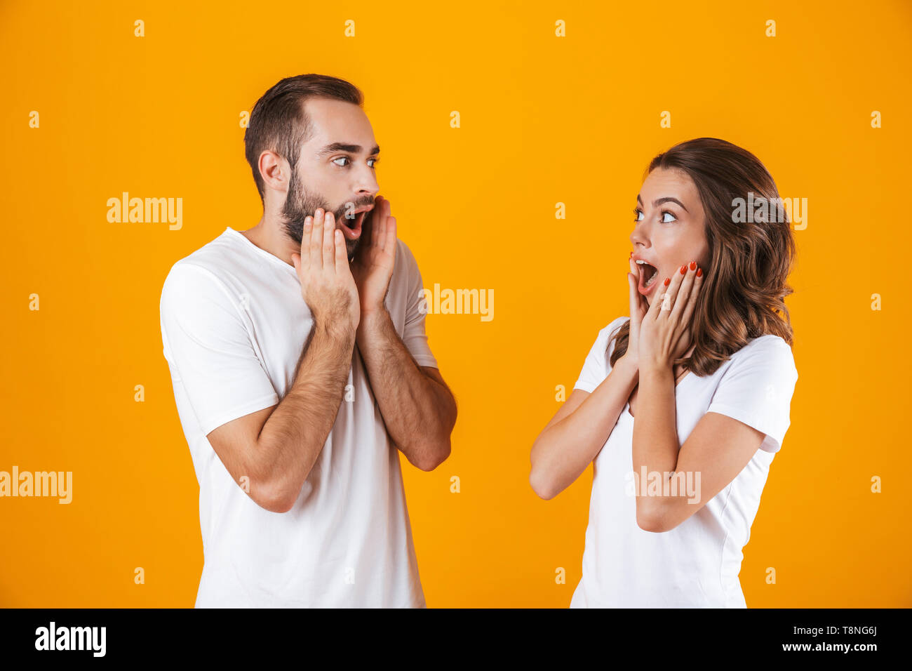 Imagen de gente guapa al hombre y a la mujer en ropa básica gritando de  placer y tocar las mejillas aislado sobre fondo amarillo Fotografía de  stock - Alamy