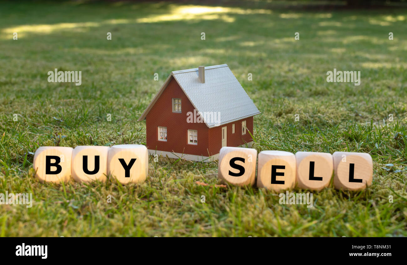 Comprar o vender una casa? Los cubos forman las palabras "comprar" y "vender" enfrente de una casa en miniatura. Foto de stock