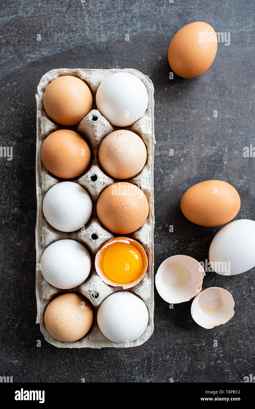Los huevos crudos orgánicos frescos, blanco, beige y marrón, uno está agrietado Foto de stock