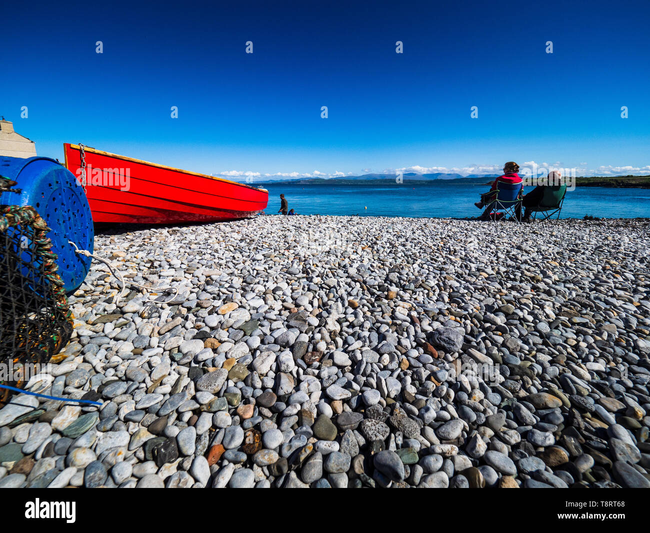 Staycation - British Vacaciones en la playa - Anglesey - playa de guijarros con barco rojo Foto de stock