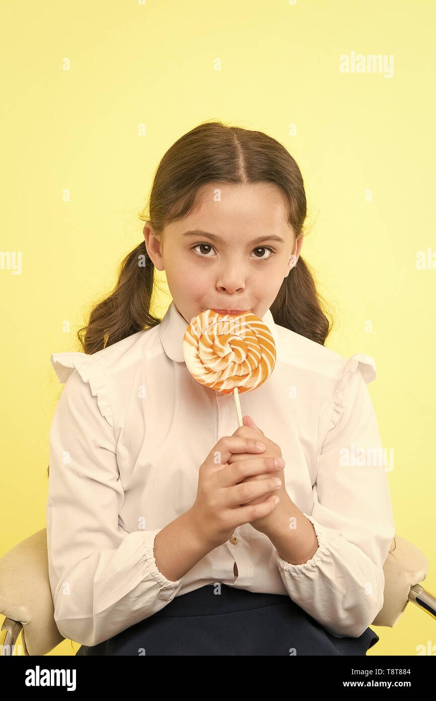 La adicción de azúcar. Chica chico lindo peinado ponytails comer dulces  lollipop. Dulces en porciones adecuadas ok. Alumna uniforme escolar le  gusta dulces lollipop candy fondo amarillo. Su sabor favorito Fotografía de