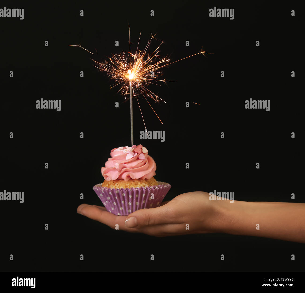 Mano femenina sosteniendo una deliciosa cupcake de cumpleaños con velas de  fuegos artificiales sobre fondo oscuro Fotografía de stock - Alamy