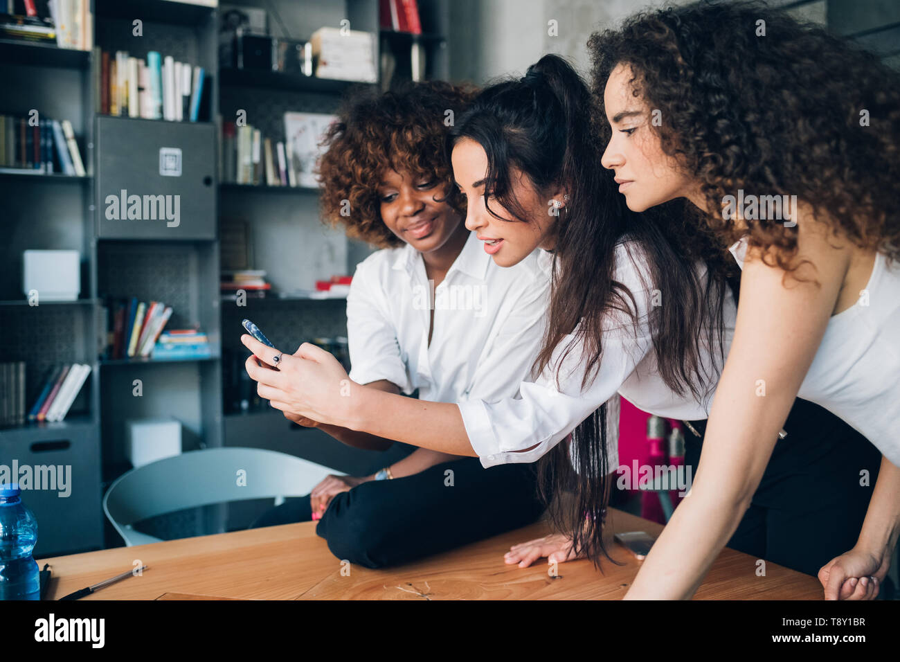 Mujeres jóvenes jugando con el smartphone en una moderna oficina - ingeniosos, creatividad, interacción Foto de stock