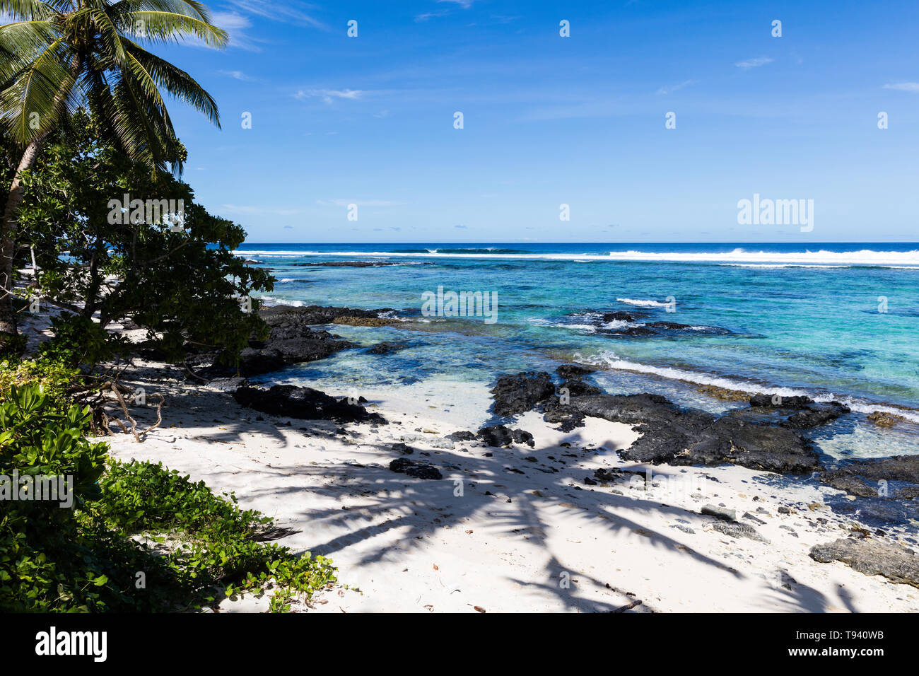 Vista paisaje tropical en la playa en la Polinesia con perfecta de arena blanca, palmeras, sombra de palmeras en primer plano, el océano, con aguas color turquesa y profunda b Foto de stock