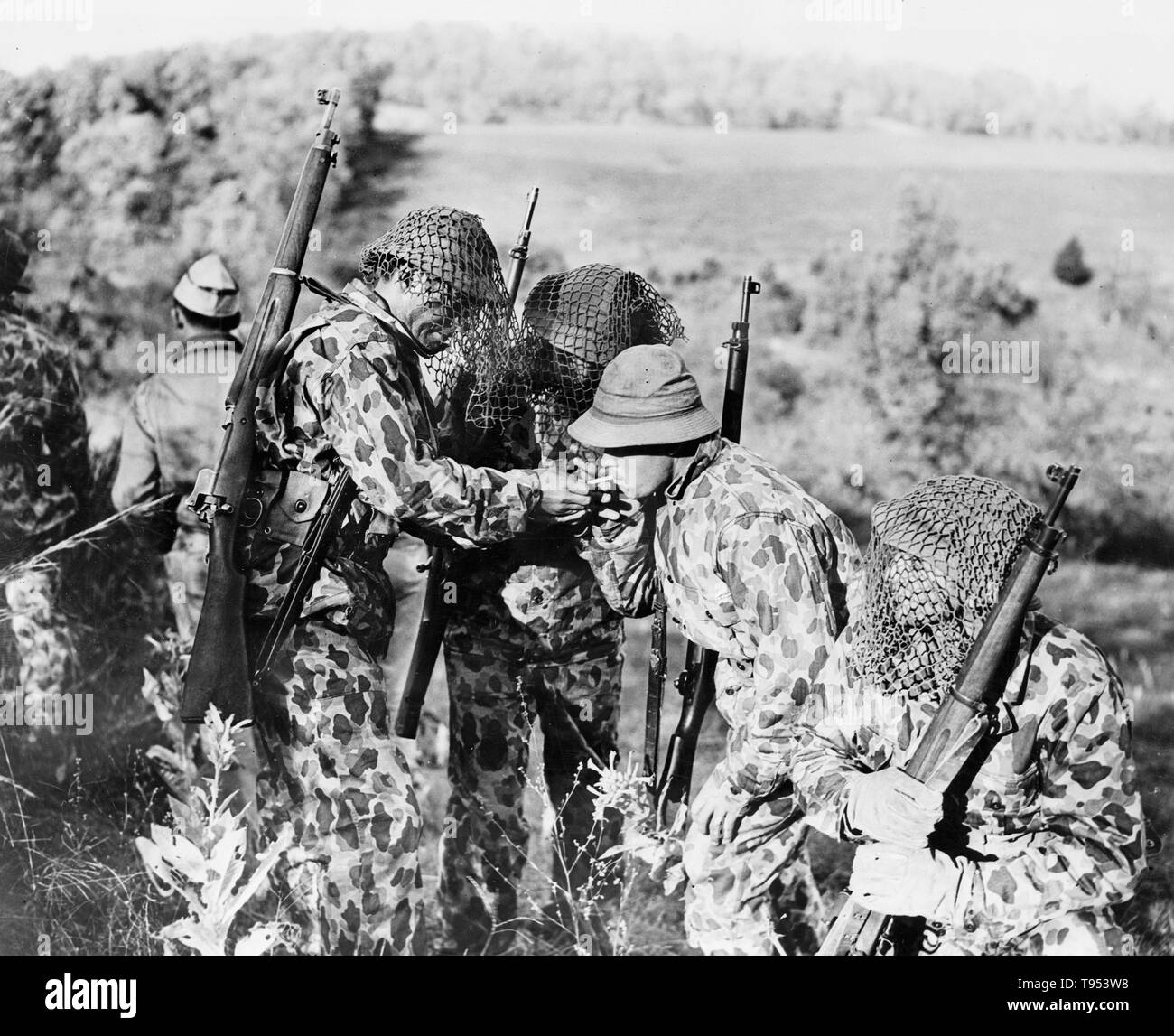 Soldados del ejército de Estados Unidos en la Segunda Guerra Mundial vistiendo uniformes camuflados para mezclarse en el paisaje y redes para ocultar sus cascos, c. 1942. Foto de stock