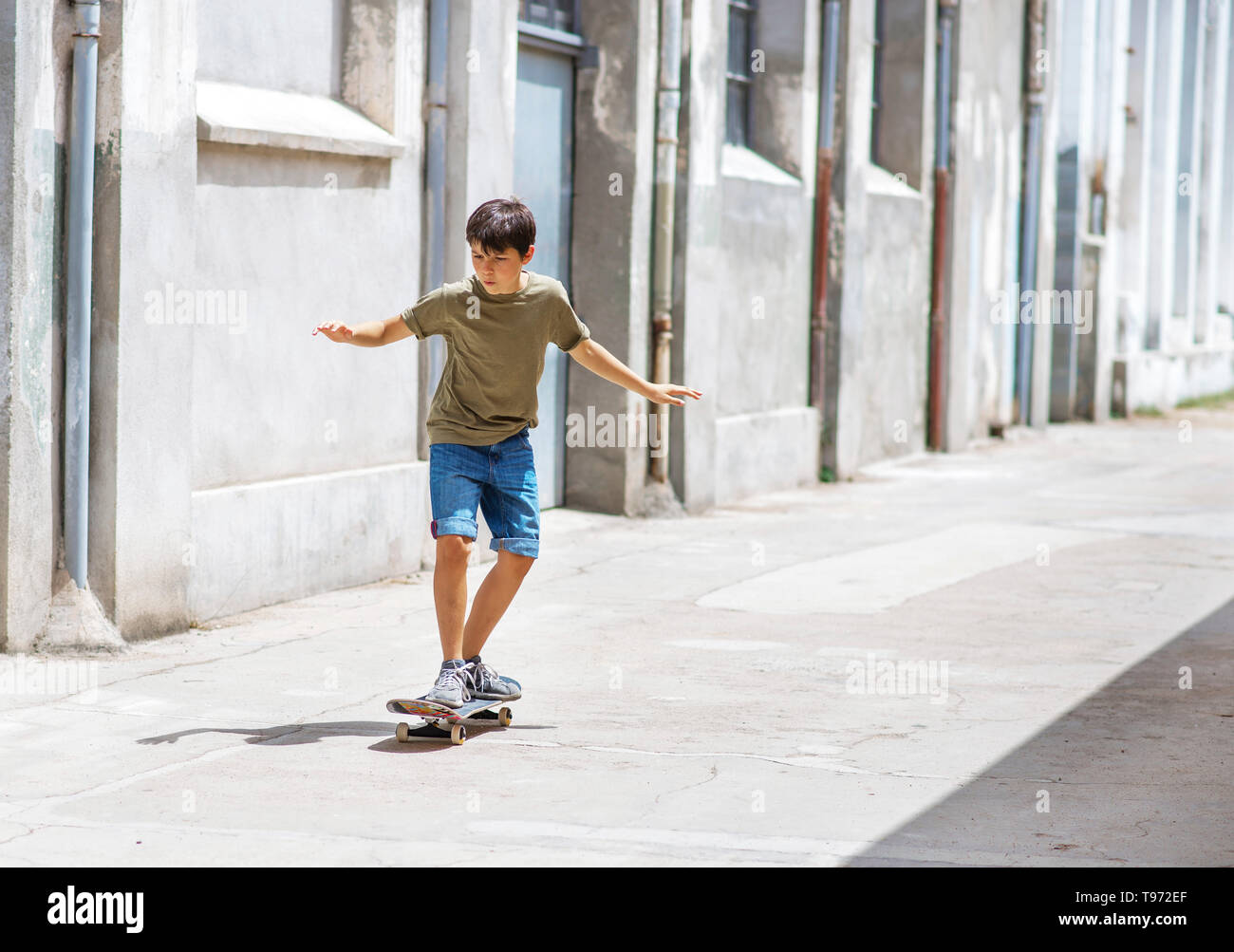 Vista frontal de un alegre skater boy a caballo en la calle en un día soleado Foto de stock