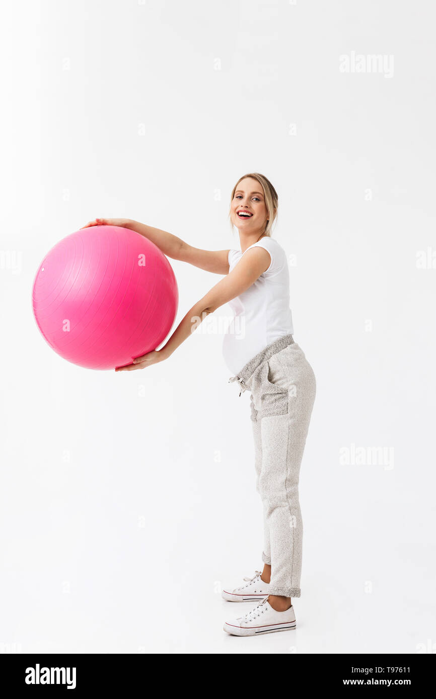 Feliz mujer embarazada levantando la pelota de ejercicios con las piernas