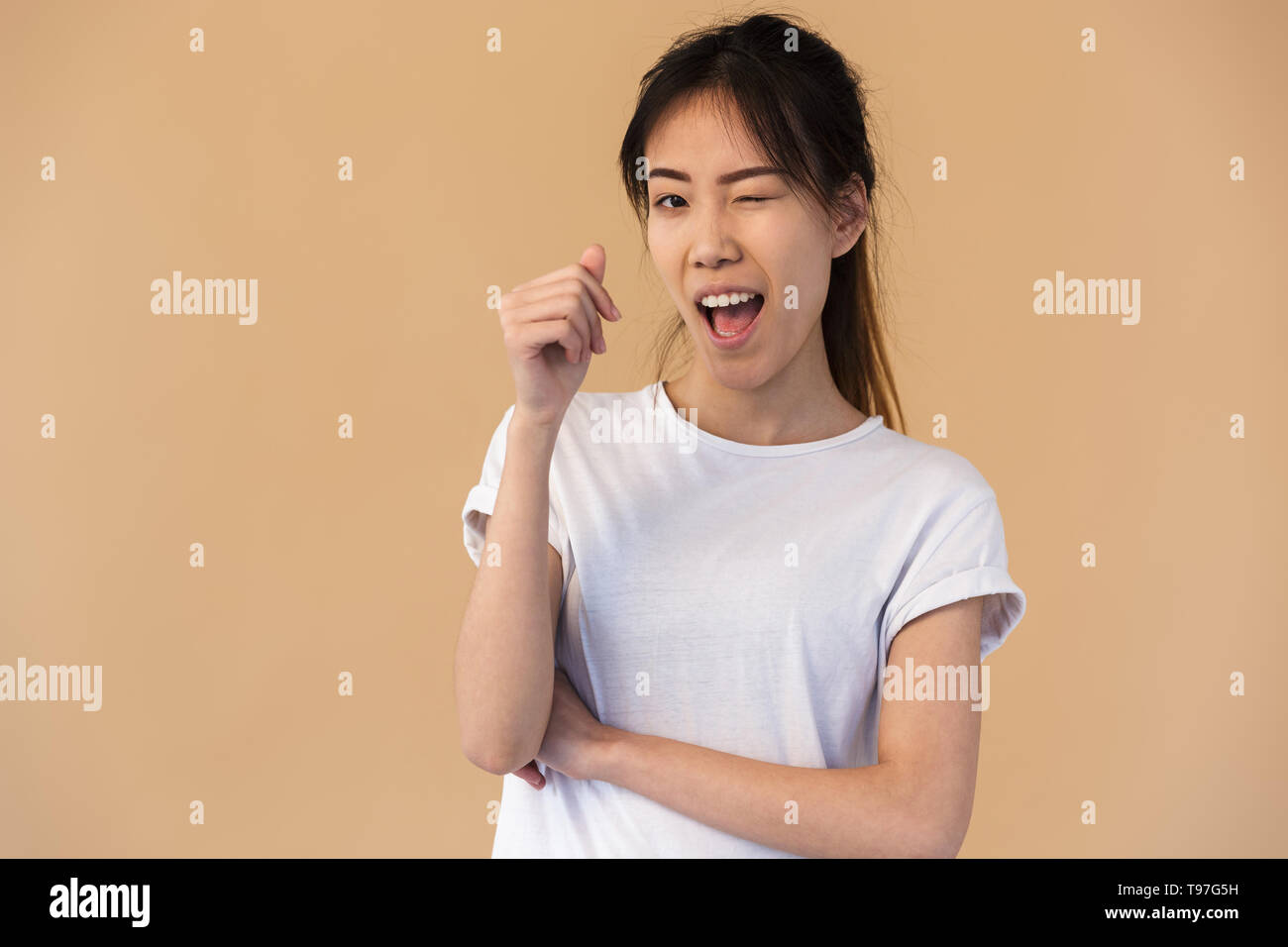 Foto de linda mujer coreana vistiendo camiseta básica y sonriente guiño a  usted aislado sobre fondo beige en studio Fotografía de stock - Alamy