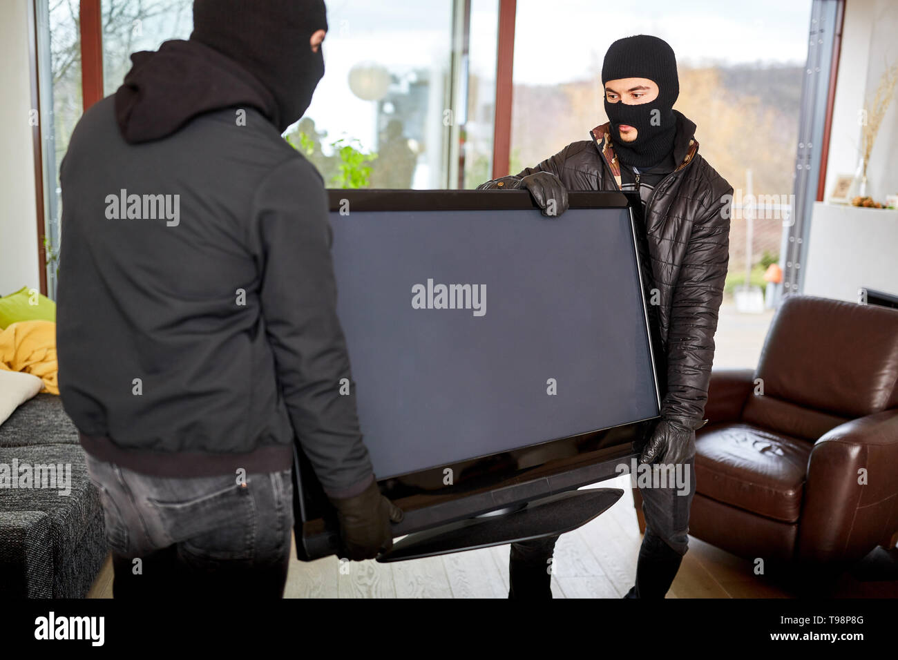 Dos encapuchados ladrones roban televisores como el botín de un salón Foto de stock