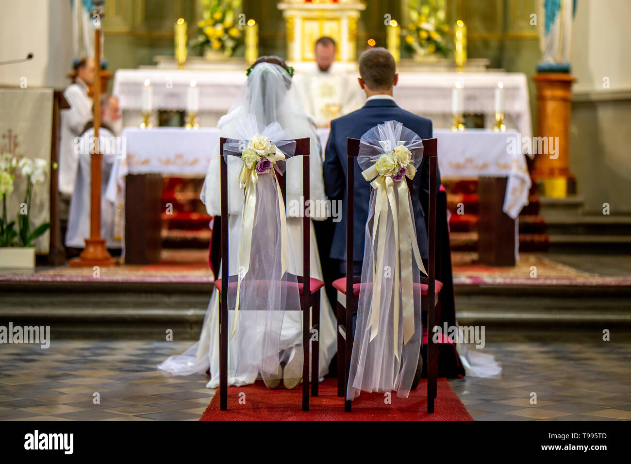 La novia y el novio durante la ceremonia en la iglesia. La novia y el novio se preparan para la comunión en las rodillas en la ceremonia en la iglesia. Sillas decoradas La novia y el novio durante la ceremonia en la iglesia. La novia y el novio se preparan para la comunión en las rodillas en la ceremonia en la iglesia. Sillas decoradas