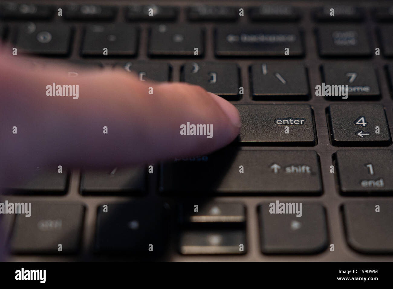 Dedo humano que está presionando la tecla Intro en un teclado de ordenador. Foto de stock