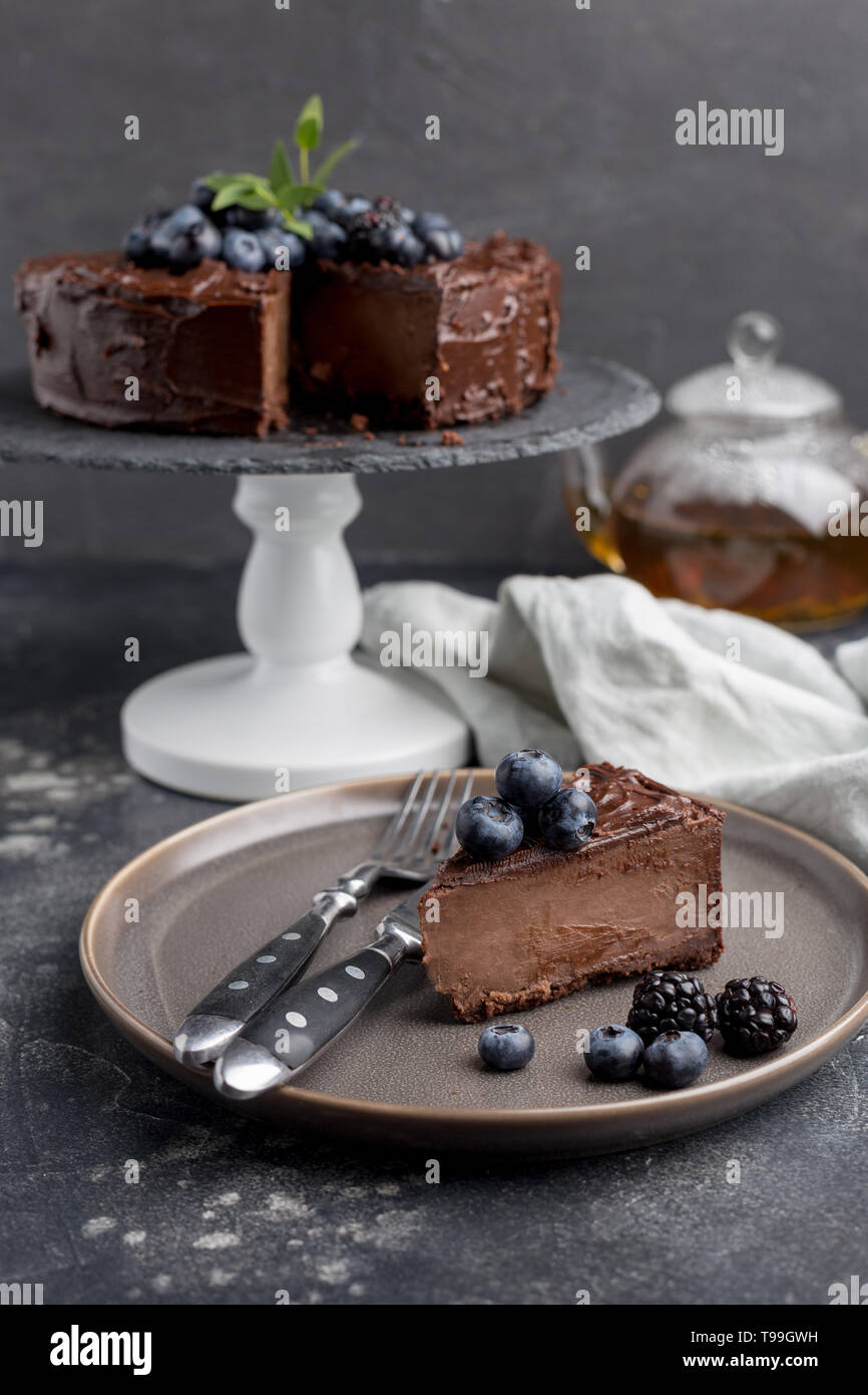 Trozo de tarta de chocolate con torta entera detrás sobre fondo gris. Concepto de vacaciones dulce alimento. Vista lateral Foto de stock