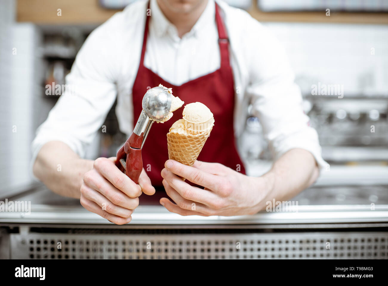 Joven vendedor poner la bola de helado en el gofre cono con herramienta  profesional en la pastelería Fotografía de stock - Alamy