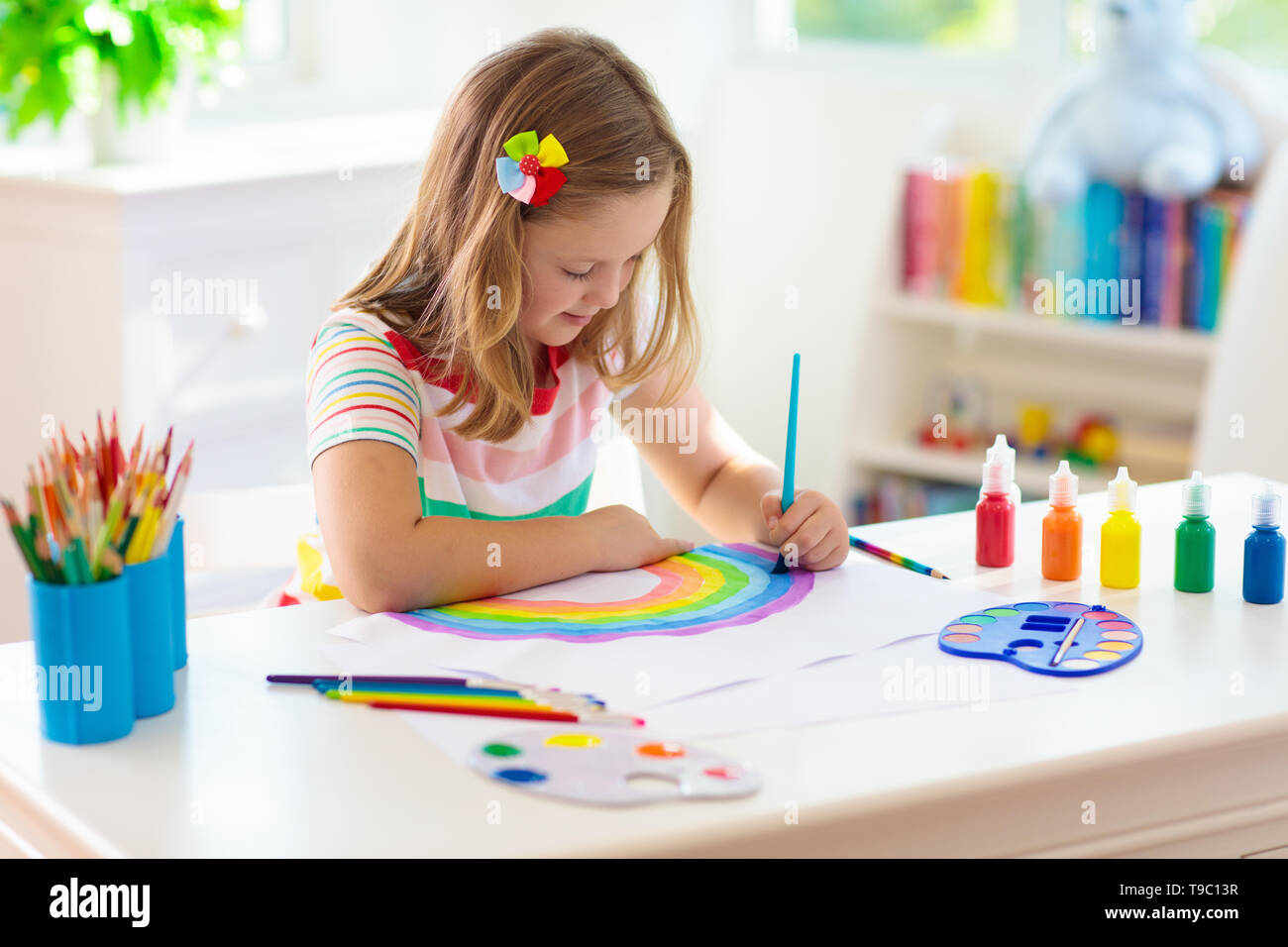 Pintura para niños. Pintura Infantil en blanco soleada sala de estudio. Dibujo  de niña arco iris. La escuela kid haciendo arte deberes. Artes y oficios para  niños. Pintura en c Fotografía de