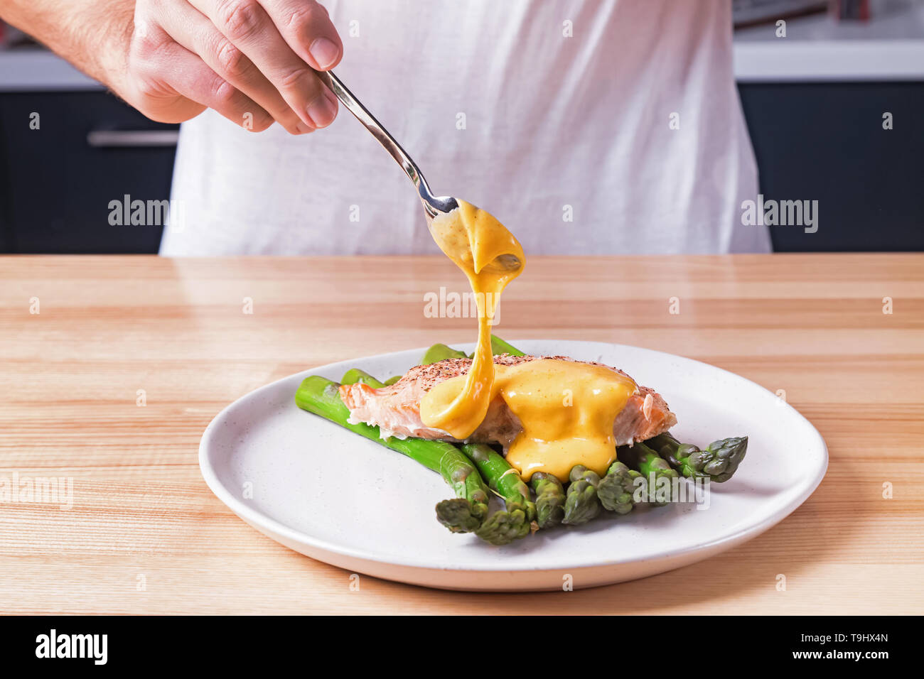 Las manos del hombre verter la salsa holandesa en la parte superior de  delicioso salmón al horno con espárragos verdes cocidos al vapor. Proceso  de preparación de la presentación de la comida