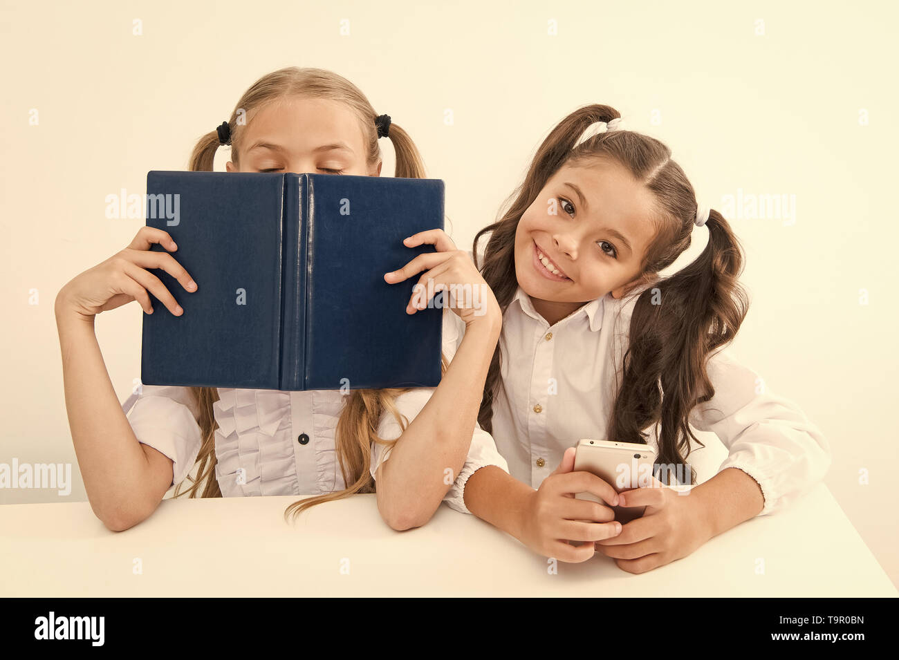 Contra la vieja escuela moderna. Colegiala mantenga teléfono móvil smartphone moderno mientras su amiga disfrute de libro viejo como almacenamiento de datos analógicos. Tecnología contra e Foto de stock