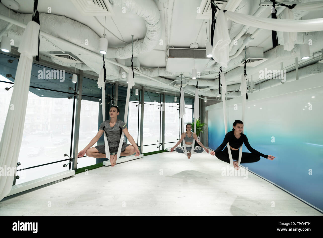 Hombre y dos mujeres disfrutando de la tranquilidad mientras practica yoga aérea Foto de stock