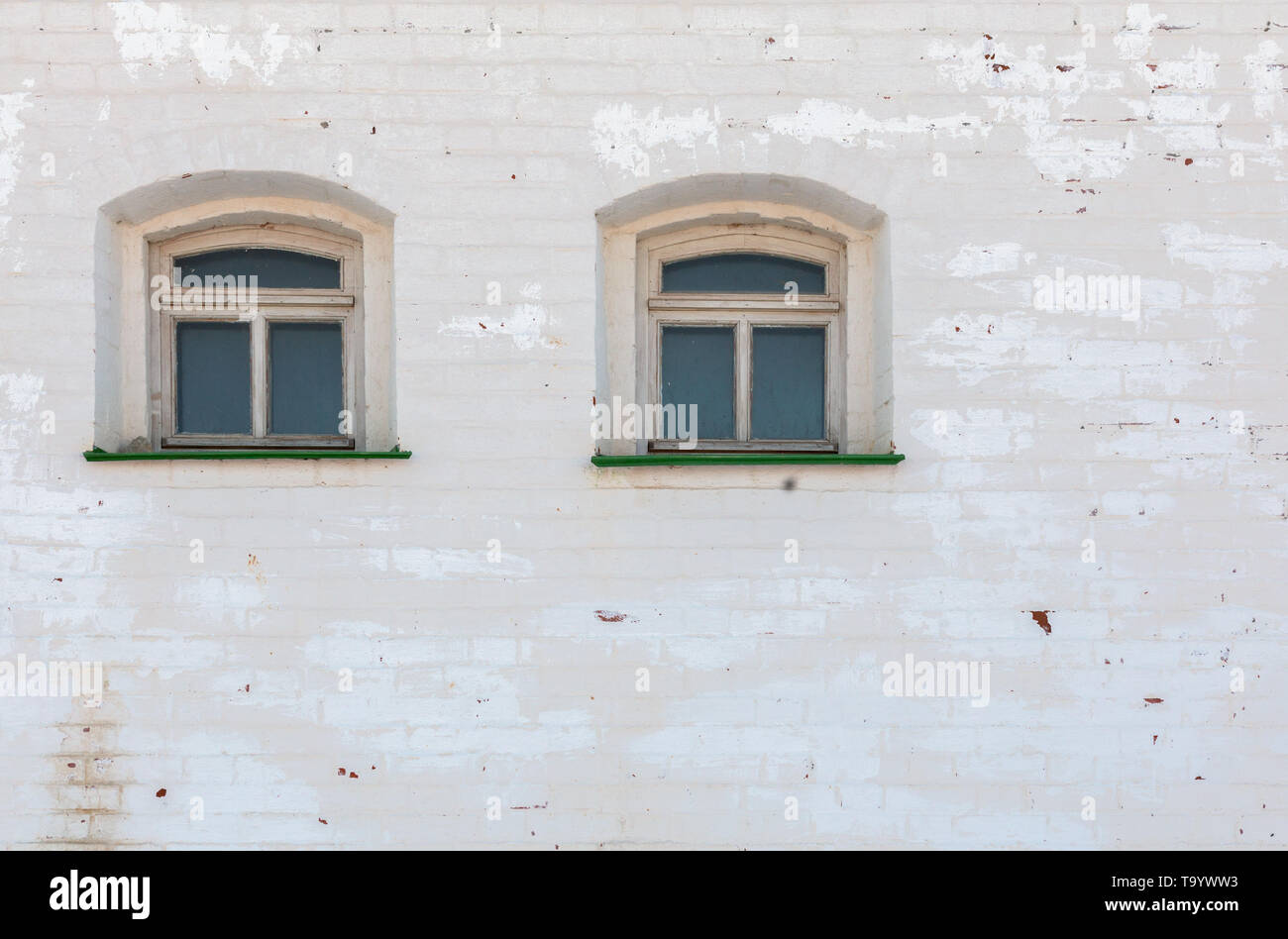 Dos ventanas en la pared bajo mediewal ladrillo espesa capa desgastada de yeso blanco. Foto de stock