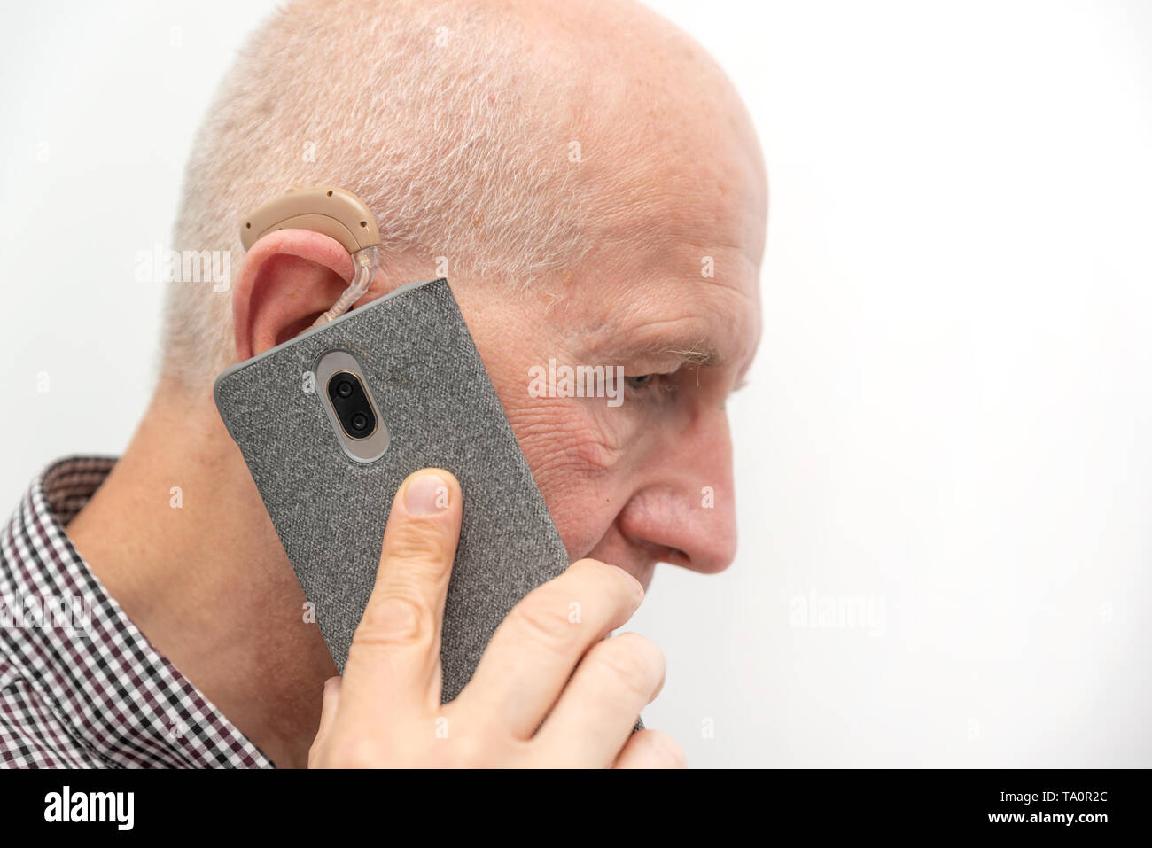 Audífono en el oído del anciano hombre viejo. Altos usando audífonos modernos mientras habla por teléfono Foto de stock