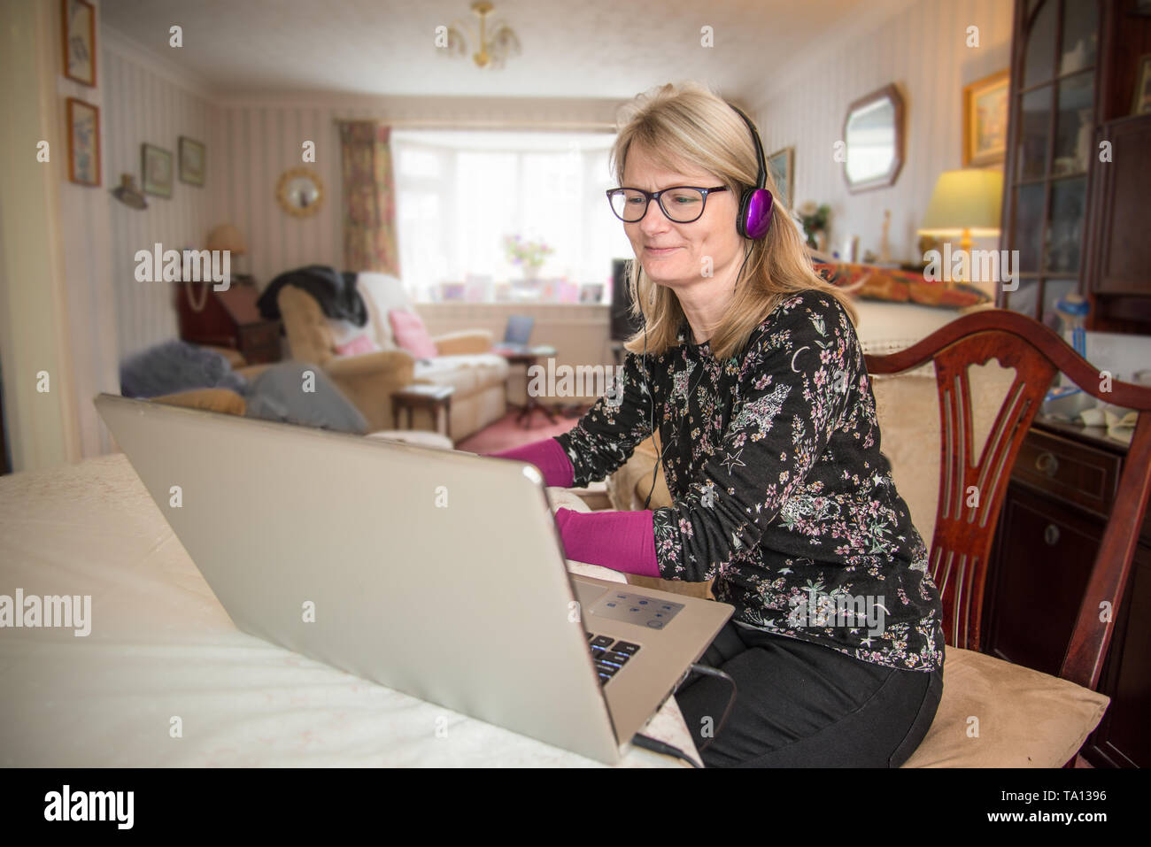 Una madre que trabaja en casa,online con su ordenador mirando su pantalla con interés. Foto de stock
