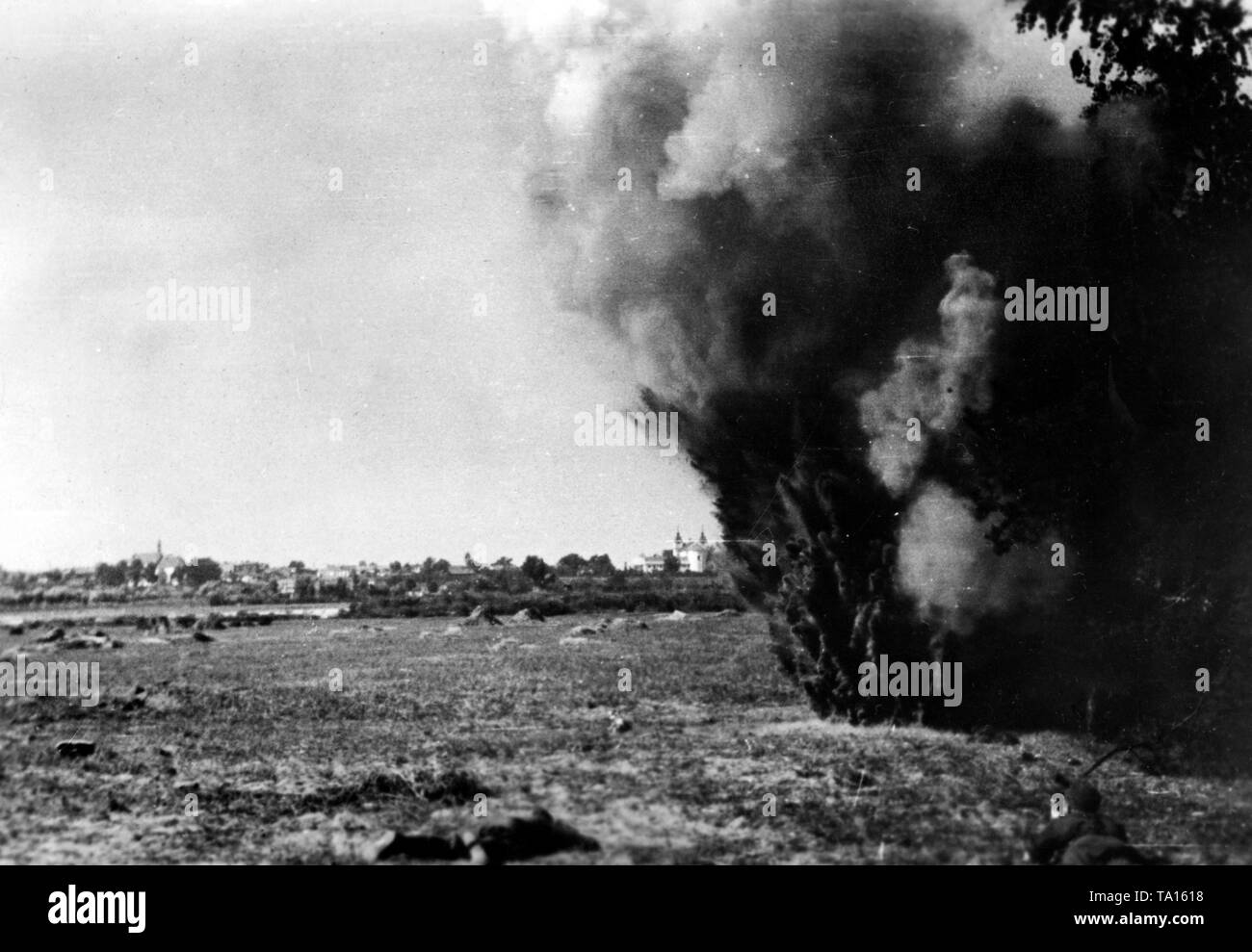 Una de las granadas de artillería soviética golpea a un campo en el sector norte del frente oriental. En el fondo, vista de la ciudad. Foto de la Propaganda Company (PK): El corresponsal de guerra Moeller. Foto de stock