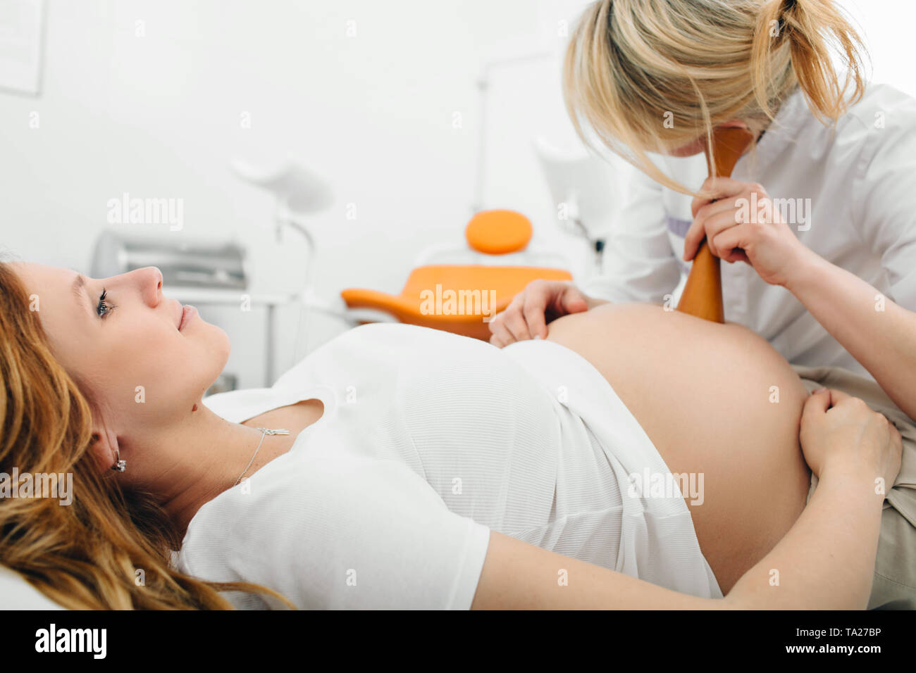 Mujer embarazada tras examen por su obstetra. Doctora escuchando embarazada vientre con equipo médico especial Foto de stock