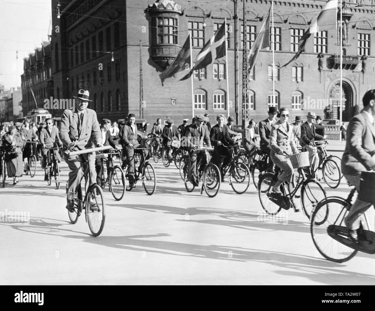 Hombres y mujeres, obreros y empleados, paseo con sus bicicletas en su tiempo libre por la tarde en la plaza del ayuntamiento de Copenhague. En el fondo del ayuntamiento. Foto de stock