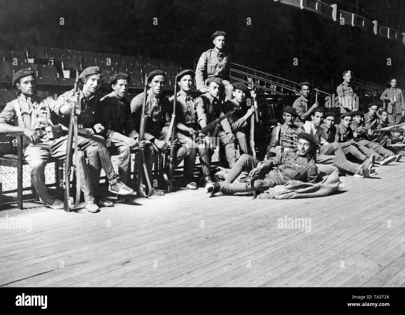 Foto de un grupo de soldados españoles en un teatro en Zaragoza, Aragón,  España. 1936. Los soldados armados con mosquetones mentira y sentarse.  Visten uniformes, calzones con botones, boinas y alpargatas (simple