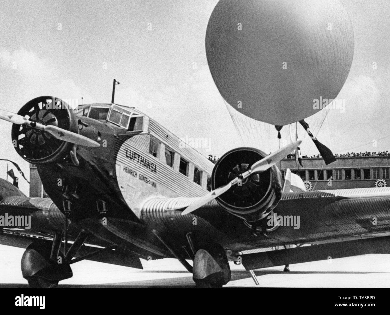 En ocasión de una exhibición aérea, un avión de transporte Ju-52 con el nombre "Heinrich Gontermann' (piloto de combate en la Primera Guerra Mundial) es en la plataforma del aeropuerto de Múnich Oberwiesenfeld. En el fondo, un gran número de espectadores en el Tribune, el cual está decorado con esvásticas. Foto de stock