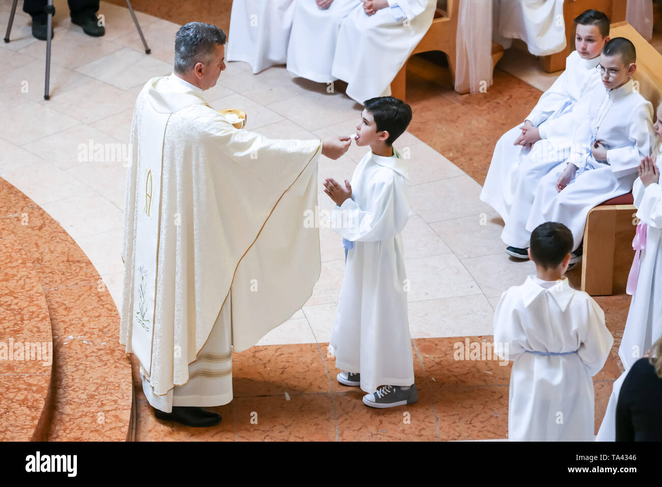 Zagreb, Croacia - El 5 de mayo de 2019 : El sacerdote da la primera comunión a los niños vestidos vestidos de blanco durante la primera comunión en la Iglesia de todos Zagreb, Croacia - El 5 de mayo de 2019 : El sacerdote da la primera comunión a los niños vestidos vestidos de blanco durante la primera comunión en la Iglesia de todos