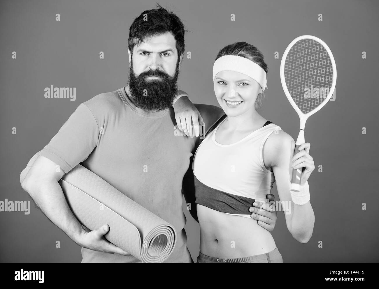Victoria y éxito. Pareja deportiva fitness entrenamiento con mat y la  raqueta de tenis. Feliz mujer y hombre barbado ejercitarse en el gimnasio.  Equipamiento deportivo. Los músculos fuertes y cuerpo. Listo para