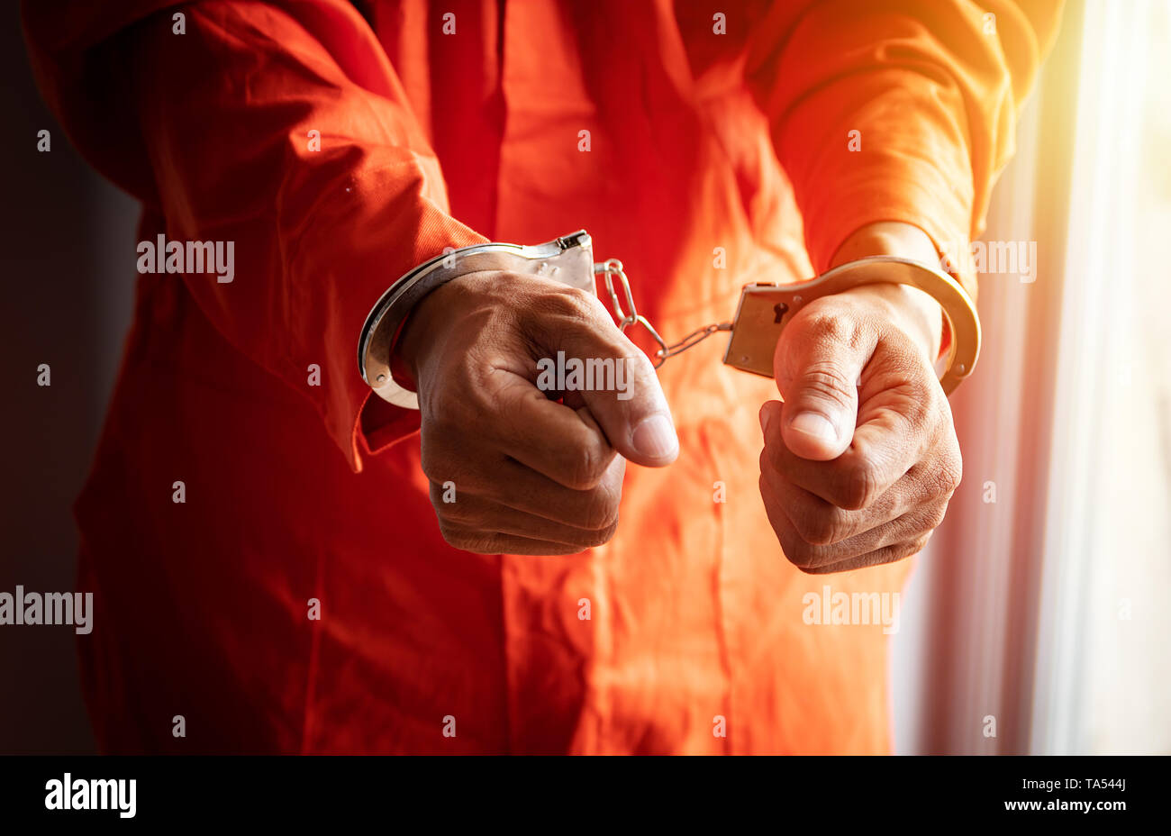 Cerca de las manos del prisionero con esposas en mono naranja en la cárcel Foto de stock